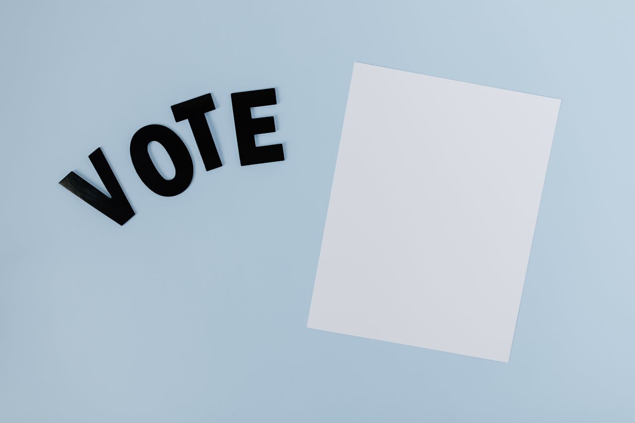 Flat lay of blank paper with VOTE letters on light blue background, ideal for election-themed content.