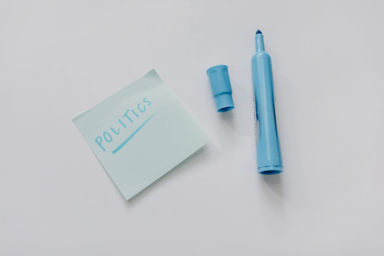 A blue marker and a note reading politics on a white surface, top view.